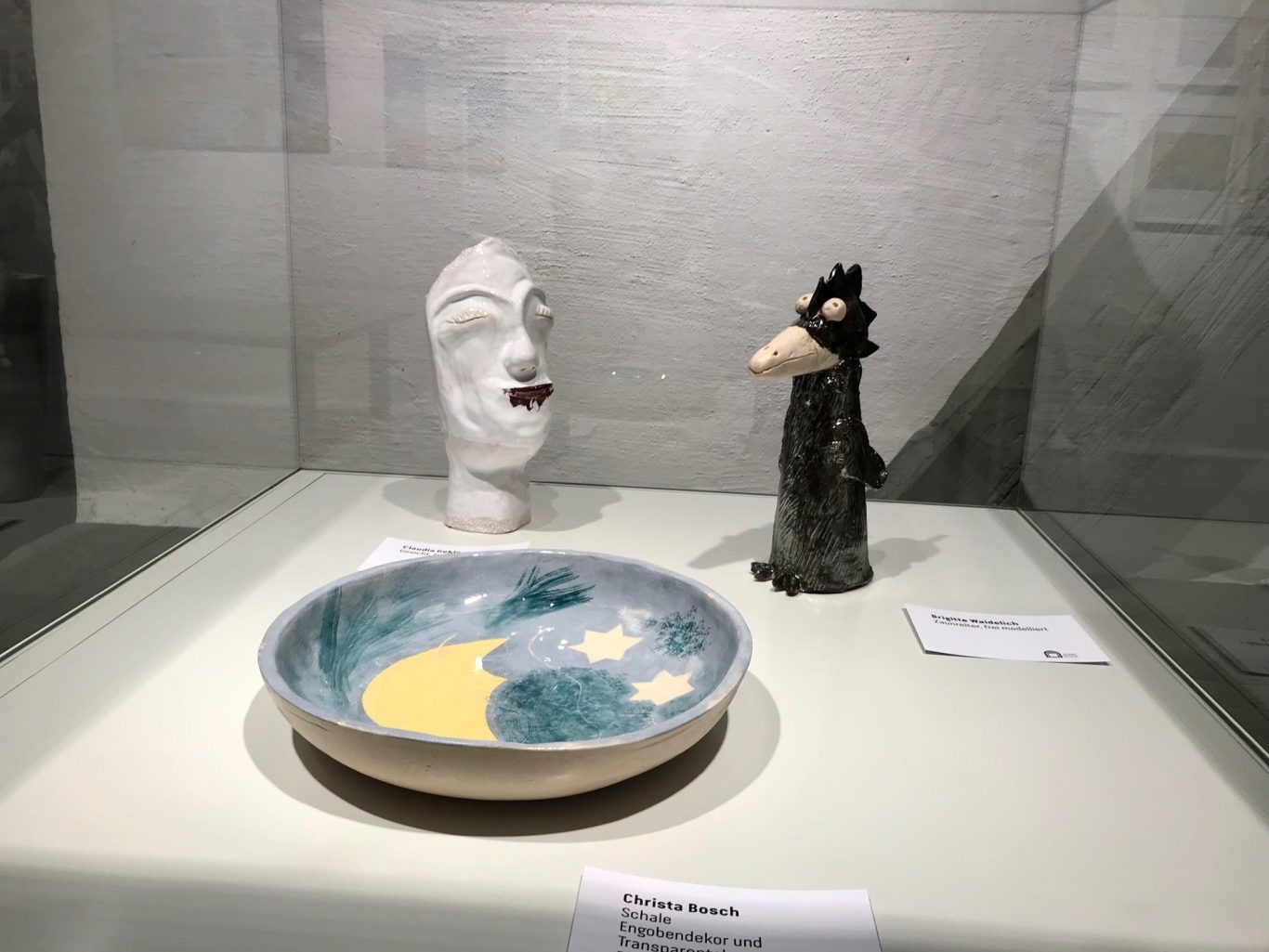 Skulptur eines Gesichts, eine schwarze Vogelfigur und eine Schüssel mit Mond und Sternen.