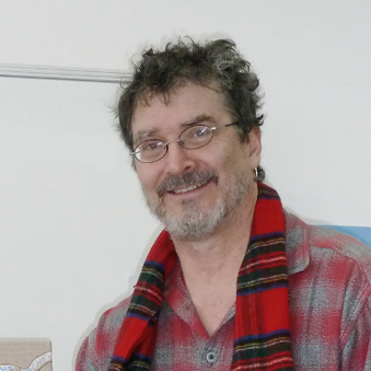 Mann mit Brille, grauen Haaren und einem karierten Hemd, lächelt freundlich.