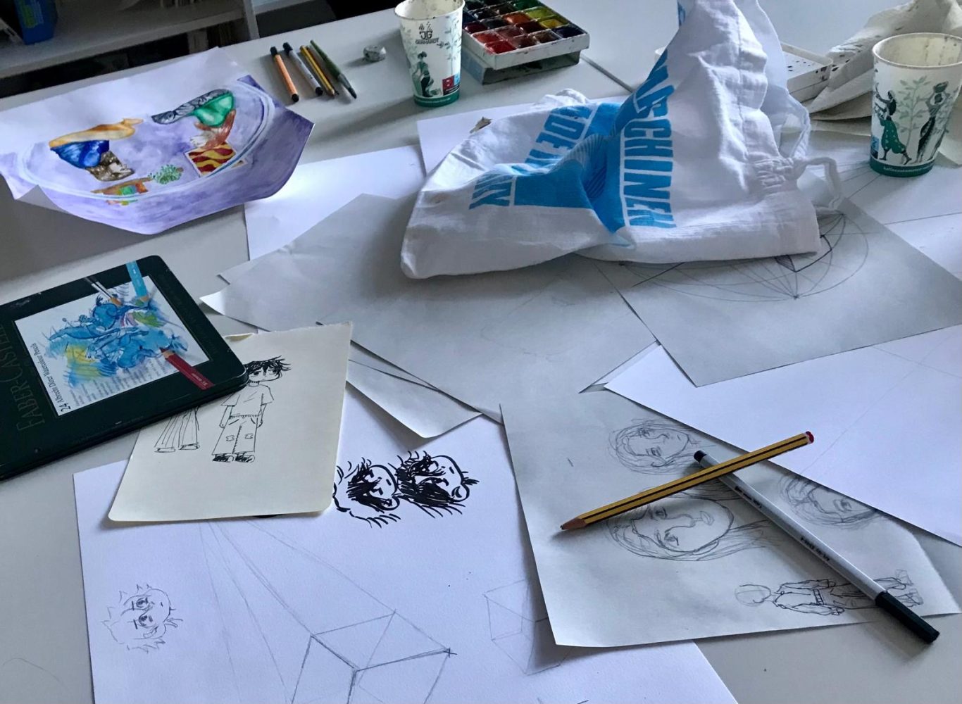 Bunte Zeichnungen, Papier und kreative Materialien auf einem Tisch verteilt.