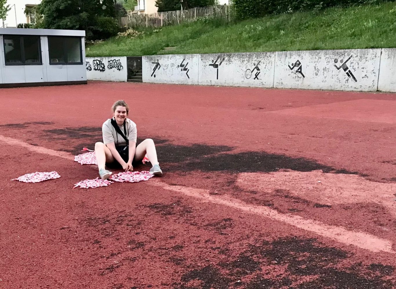 Eine Person sitzt auf einem roten Sportplatz neben pinken Abdrücken.