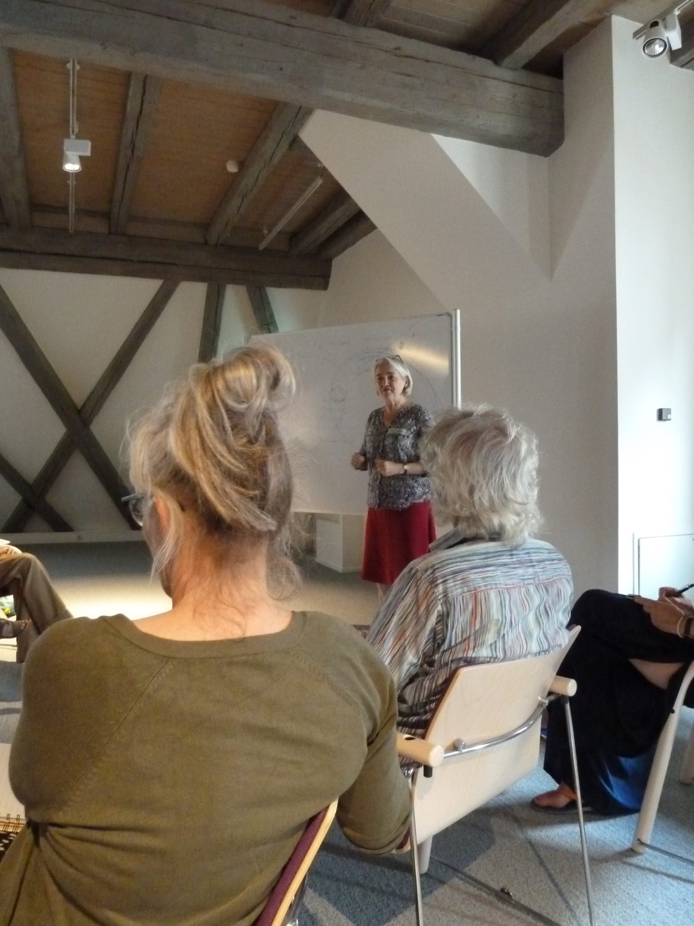 Frau mit Bluse und Rock spricht vor Publikum in einem hellen Raum.