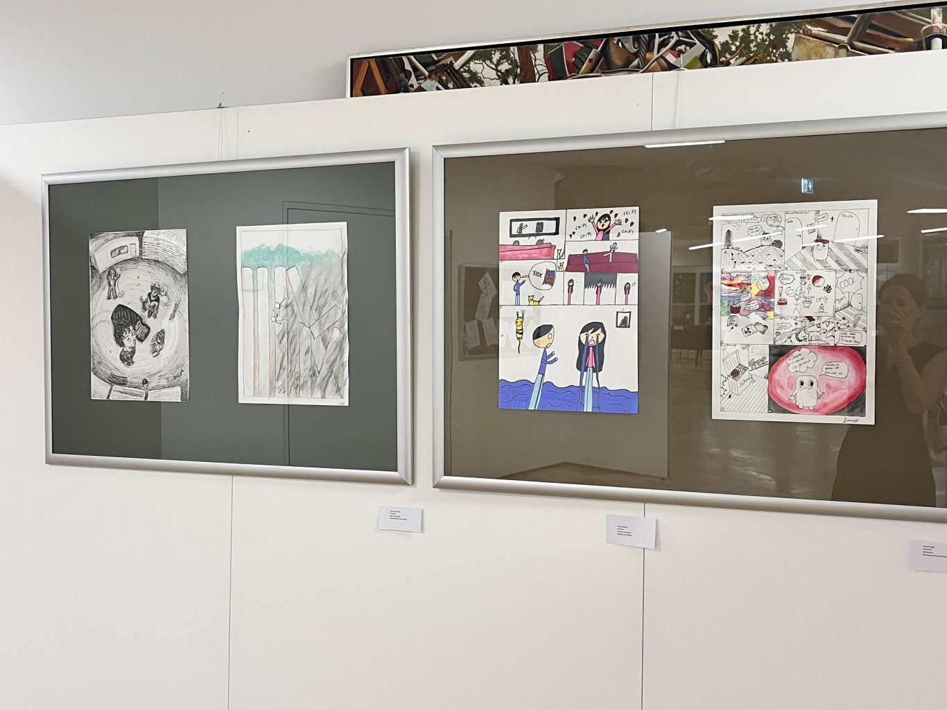 Drei gerahmte Kunstwerke an einer Wand, zwei mit bunten Illustrationen und eines in Schwarz-Weiß.