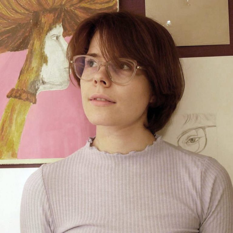 Junge Frau mit Brille, blickt nach oben, im Hintergrund Kunstwerke.