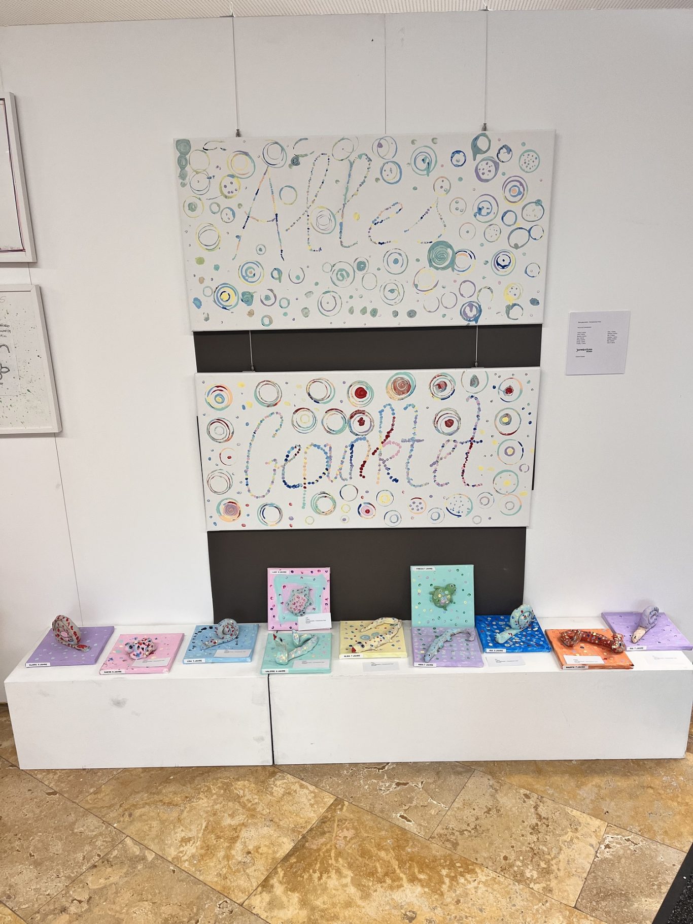 Bunte Zeichnungen an einer Wand mit mehreren Kunstbüchern darunter.