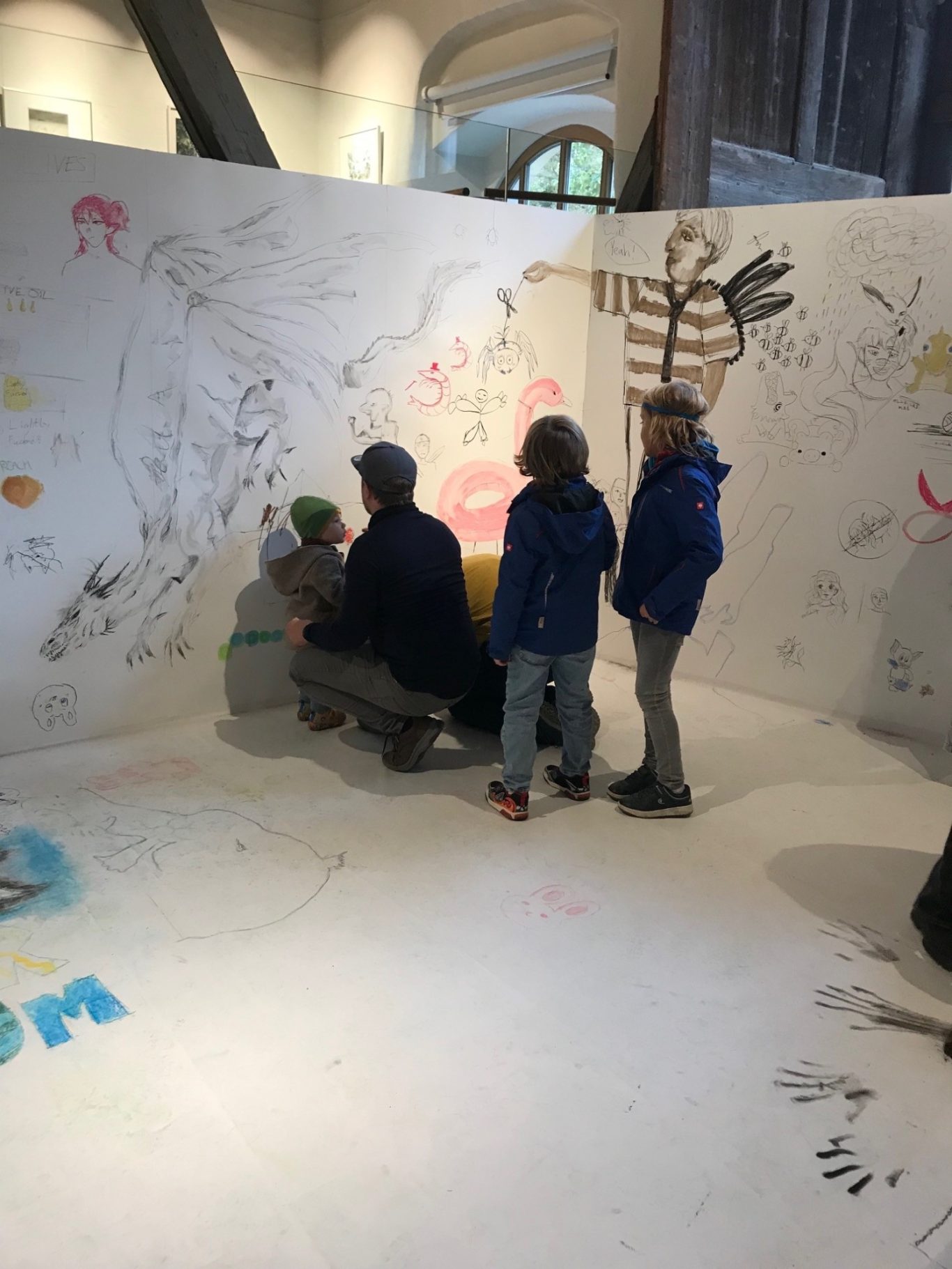 Kinder und Erwachsene zeichnen an einer bemalten Wand in einem kreativen Raum.