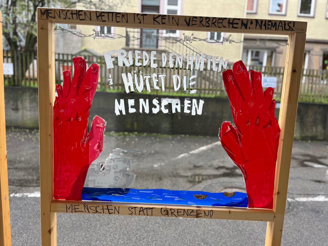 Stellwand mit einer Zeichnung mit roten Händen und einem Schriftzug.
