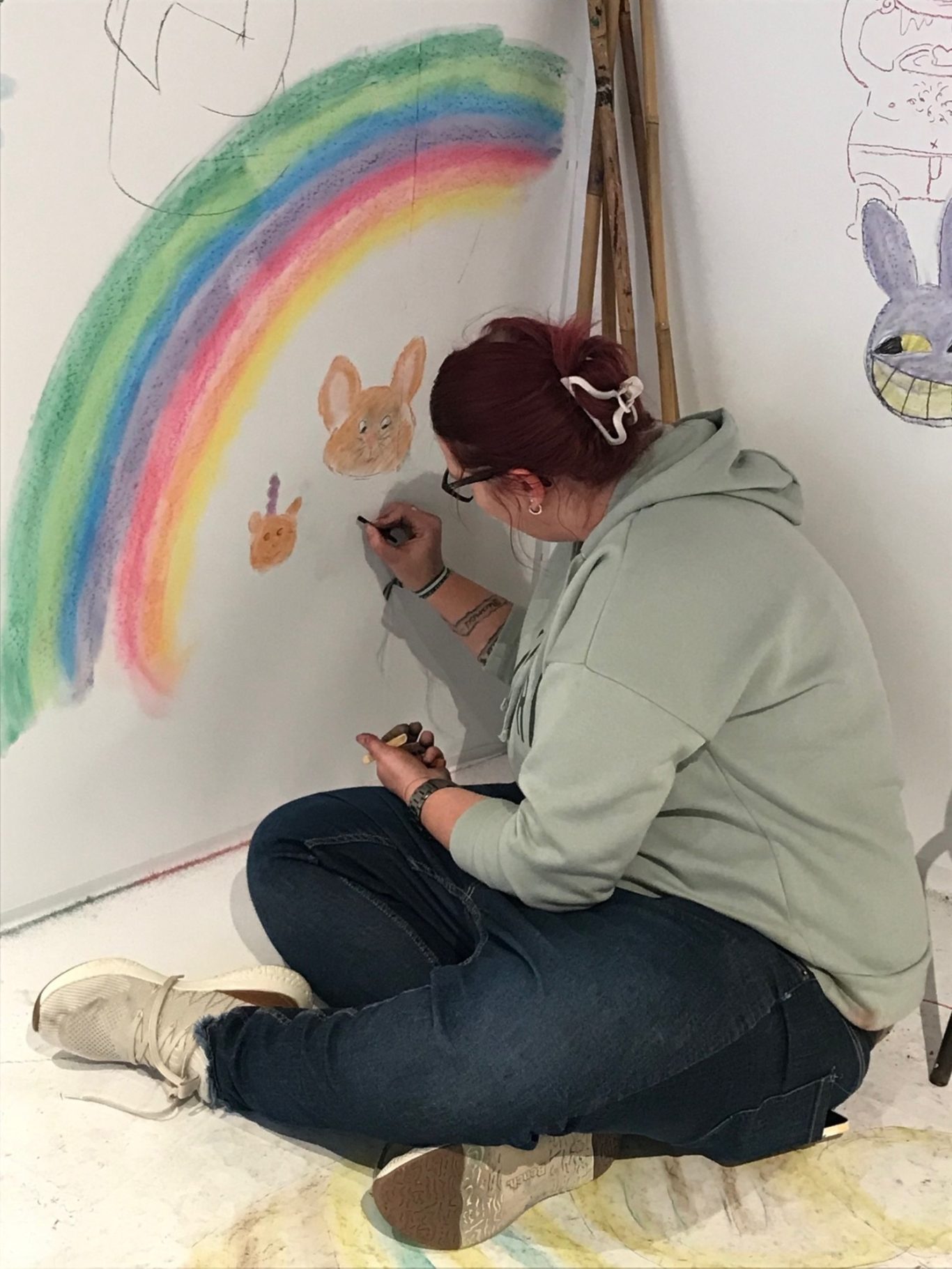 Eine Person malt an eine Wand mit einem Regenbogen und einem Tiermotiv.