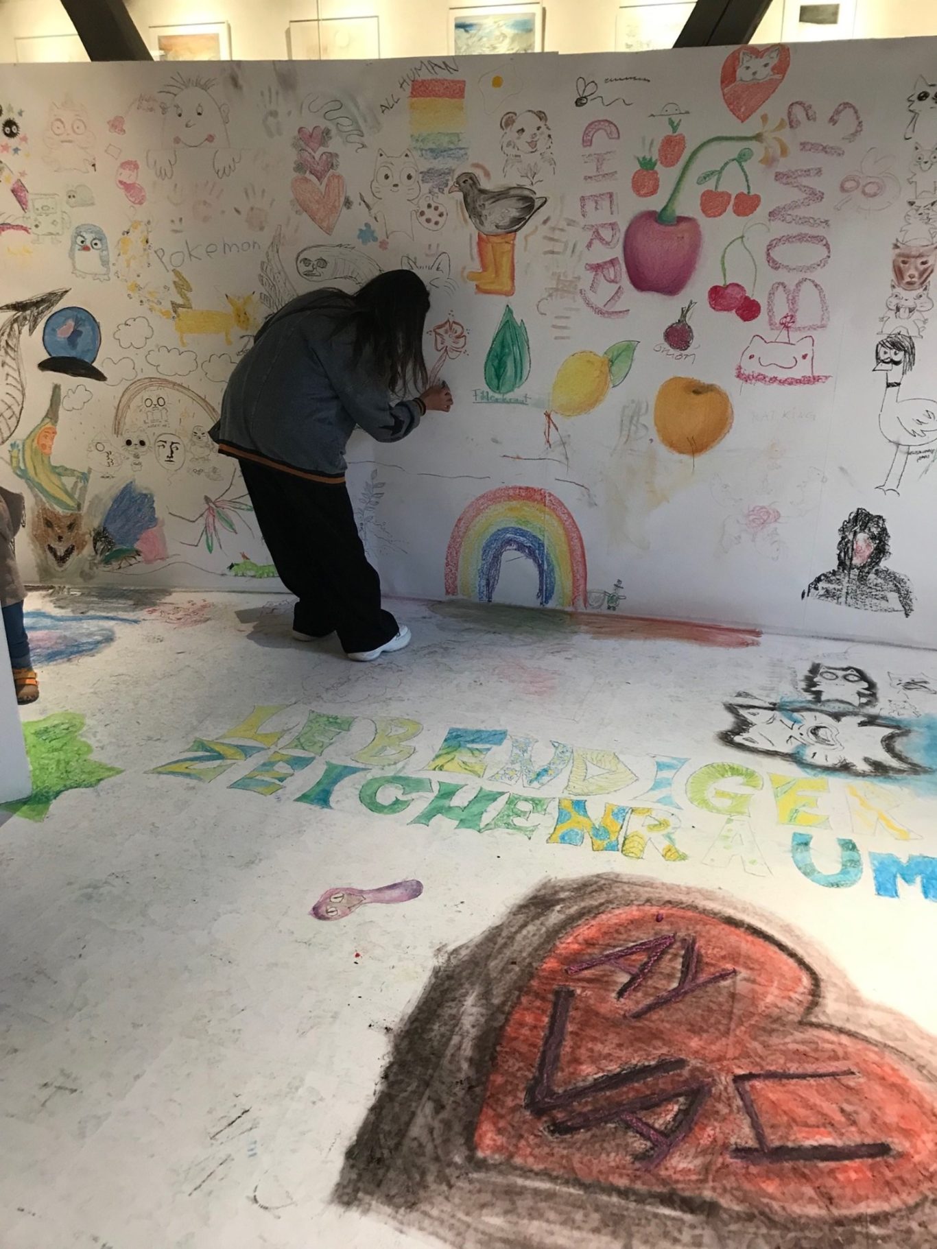 Person zeichnet bunte Grafiken an eine Wand, umgeben von künstlerischen Darstellungen.