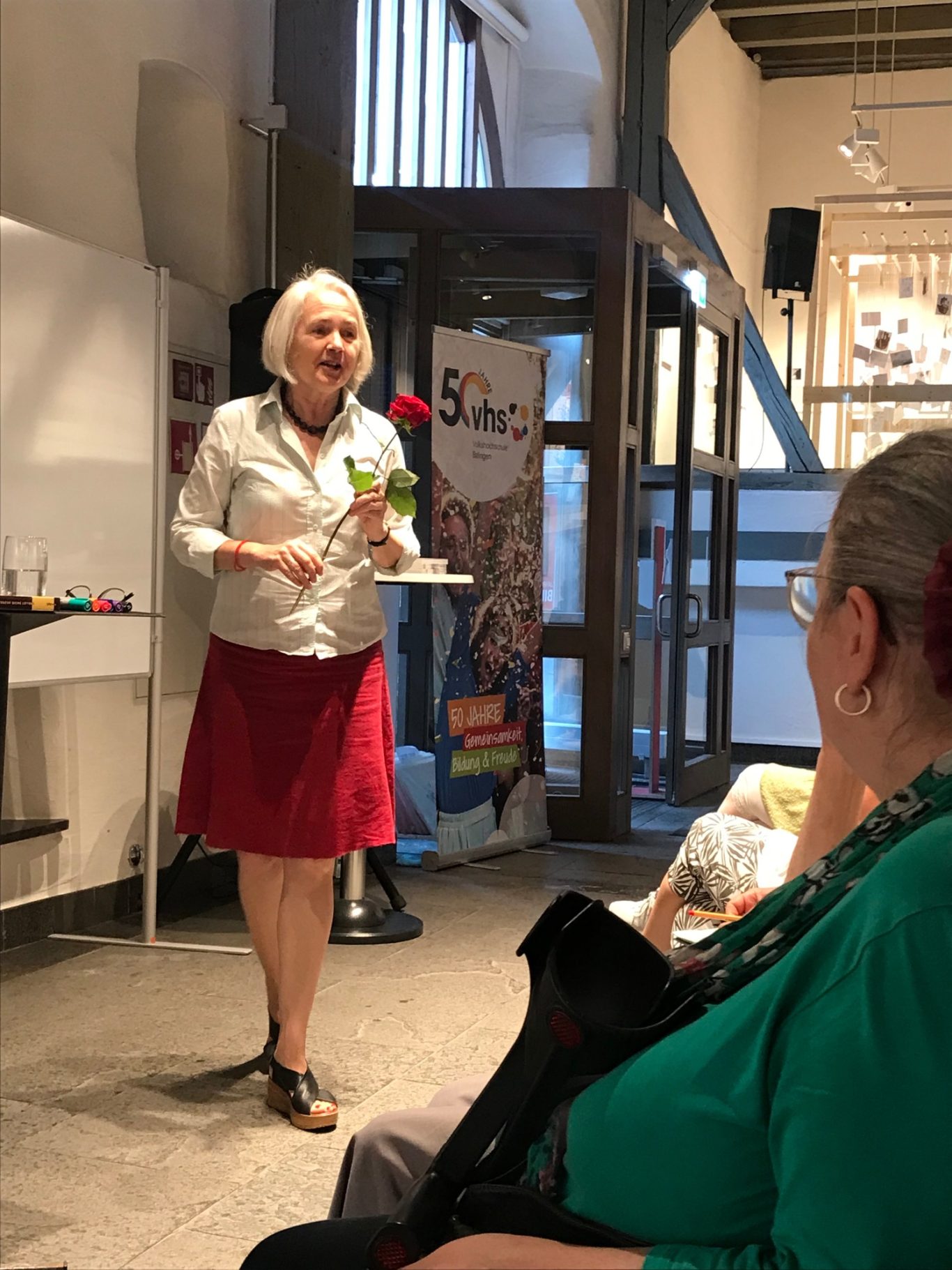 Frau Dr. Hildegard Kurt spricht vor Publikum in einem Raum und hält eine rote Rose in der Hand.