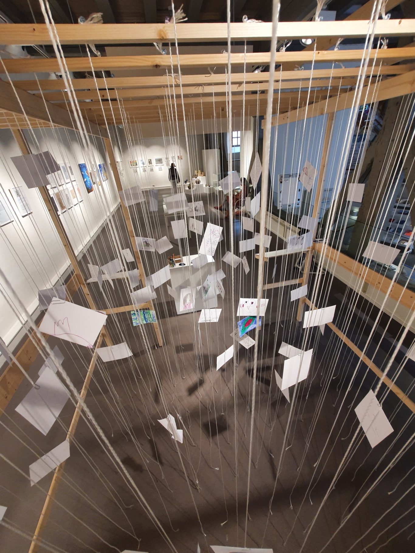 Hängende Karten und Blätter in einer Galerie, von einem Holzrahmen gehalten.