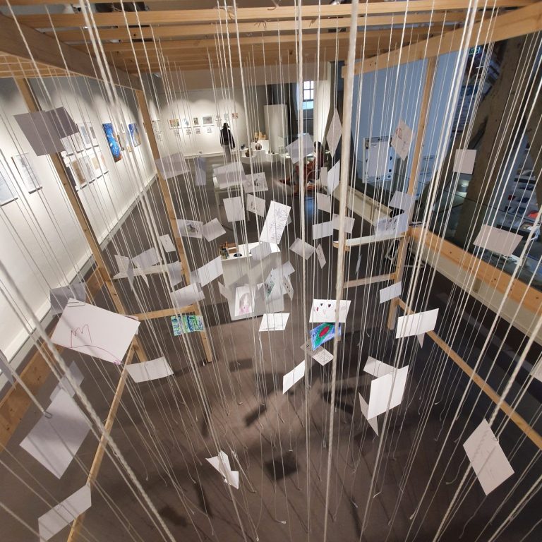 Kunstinstallation mit schwebenden Blättern in einem hellen Ausstellungsraum.