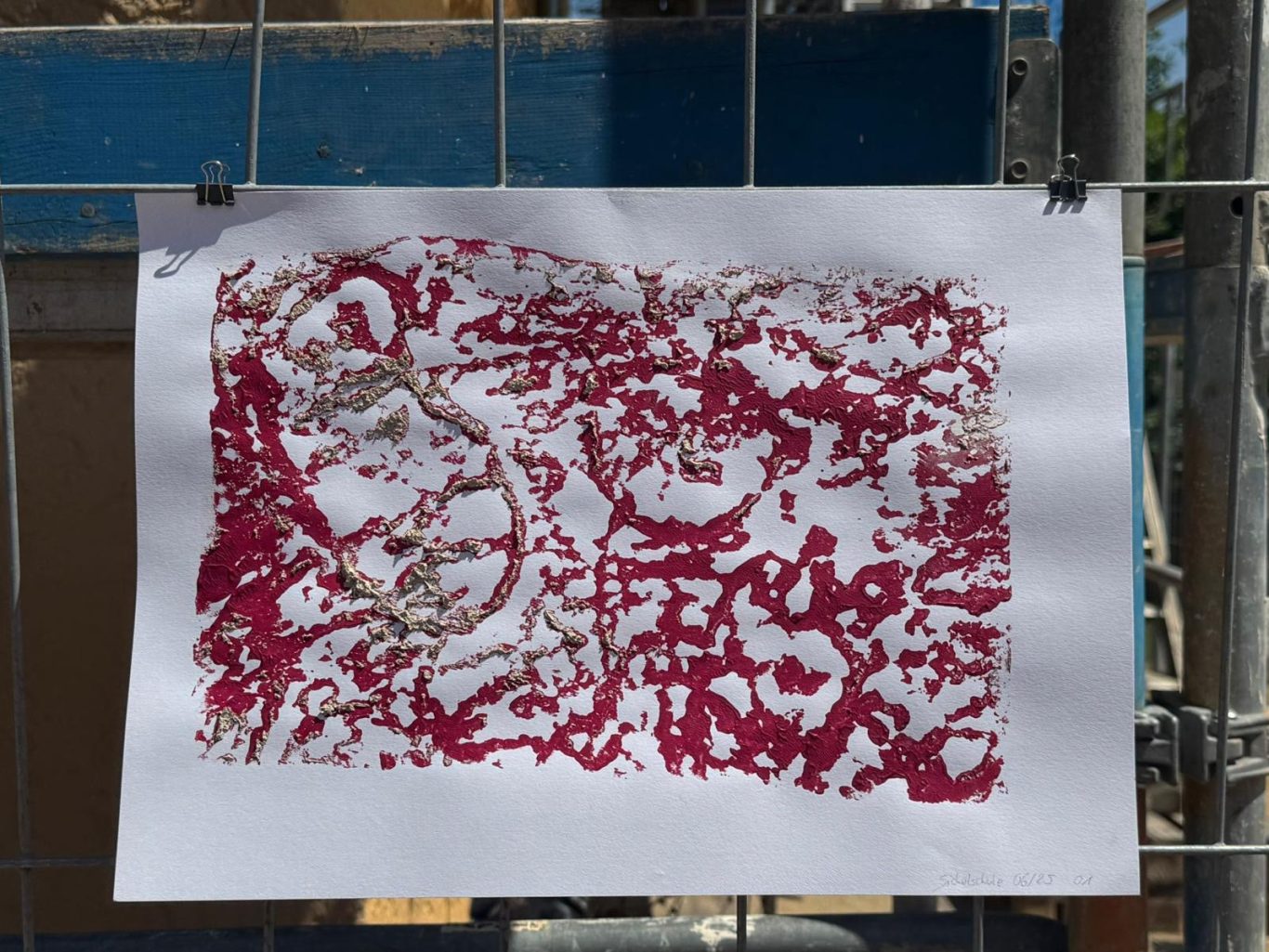 Kunstwerk mit rot-weißen Mustern, auf Papier gedruckt und an einem Zaun befestigt.