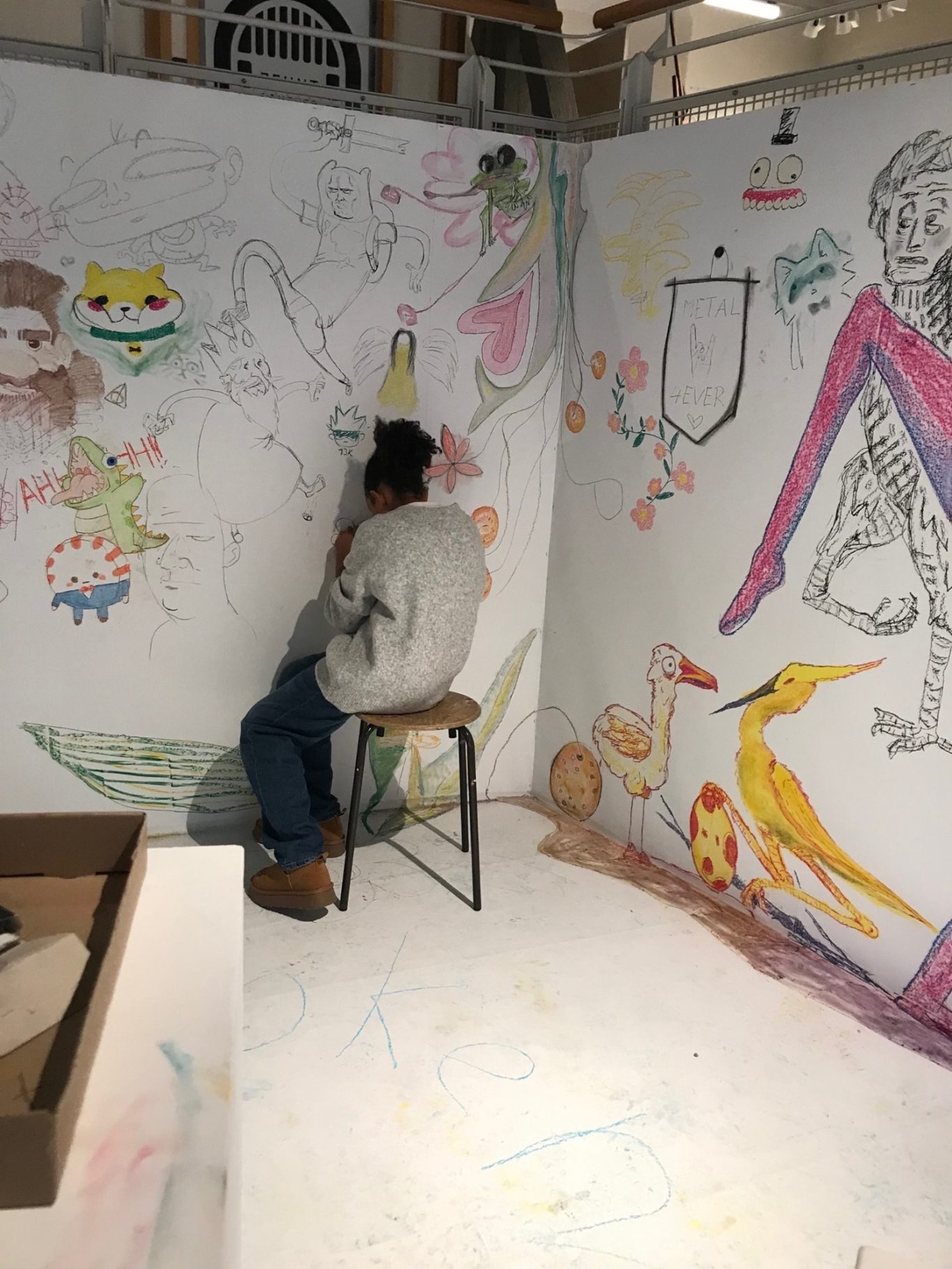 Person sitzt auf einem Hocker und malt bunte Zeichnungen an einer Wand.