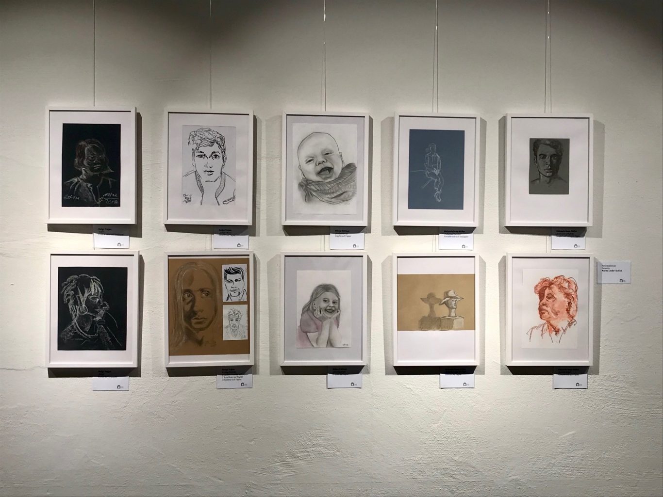 Eine Galerie mit zehn gerahmten Zeichnungen an einer Wand.