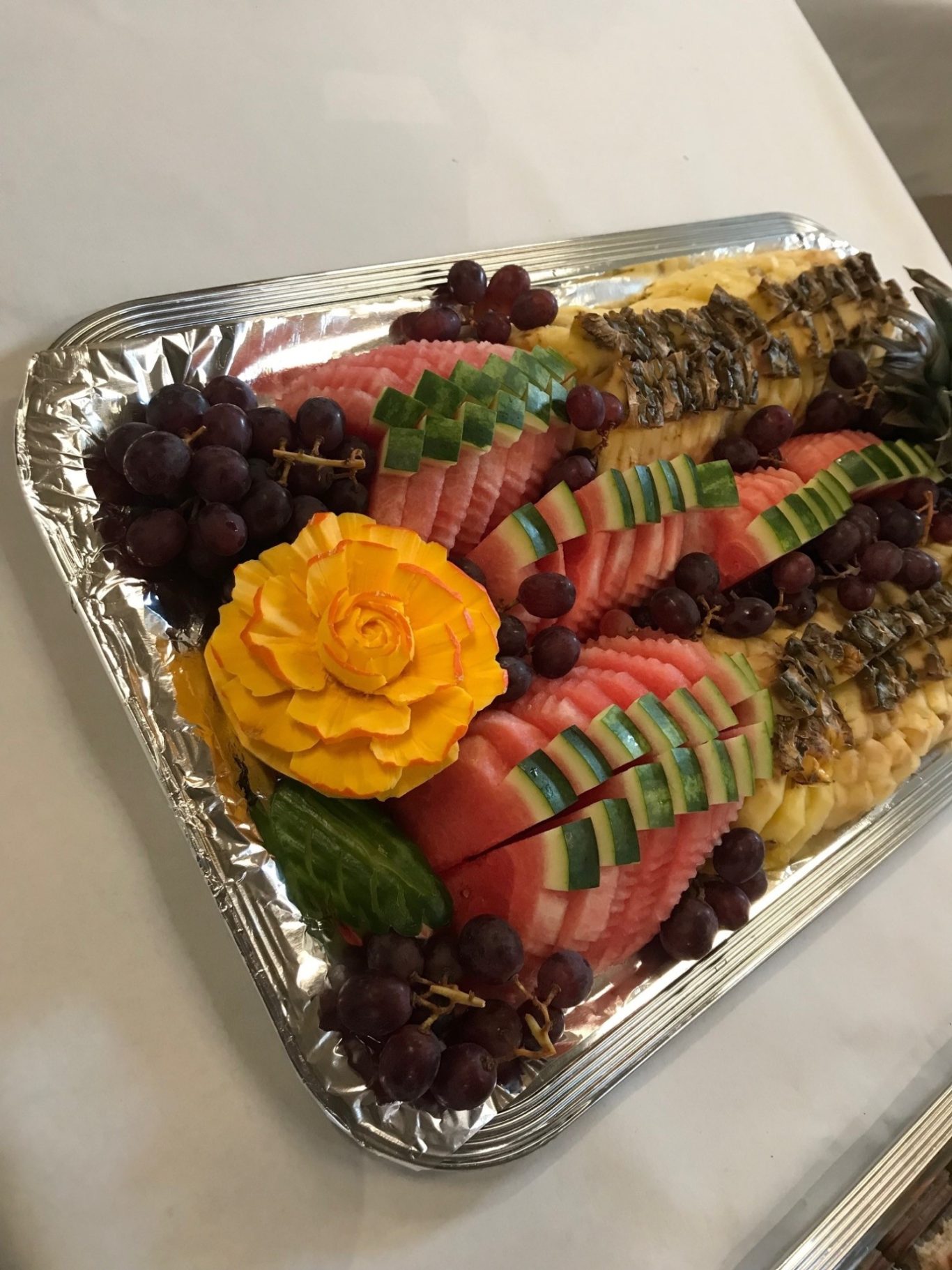 Eine Platte mit kunstvoll geschnitztem Obst, darunter Melonen, Trauben und eine Blüte.