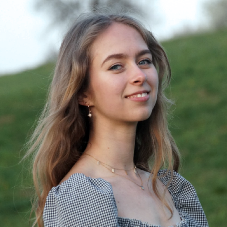 Junge Frau mit langen Haaren, lächelnd vor grünem Hintergrund.