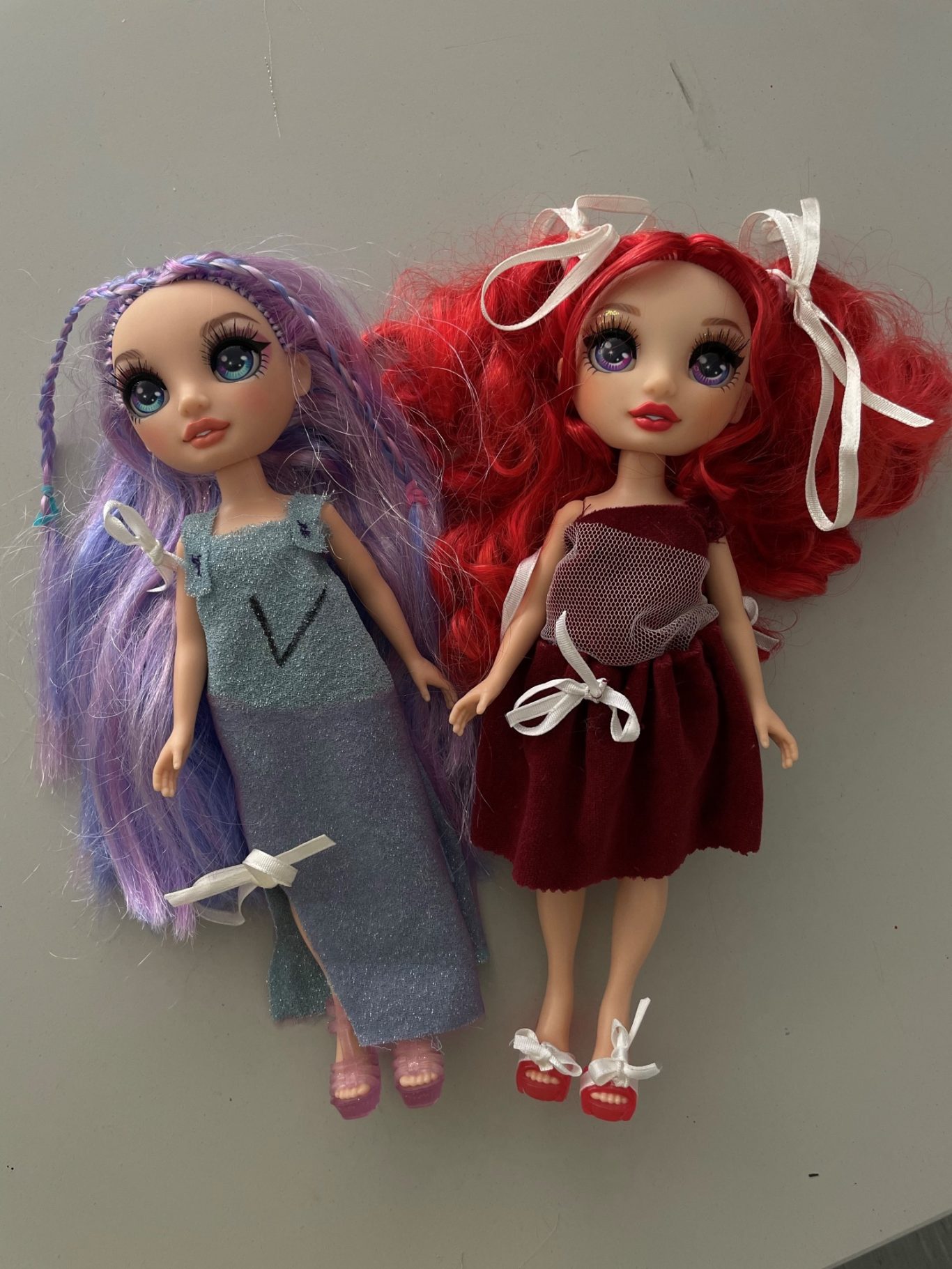 Zwei Puppen mit langen Haaren, eine lila und eine rote, im festlichen Outfit.