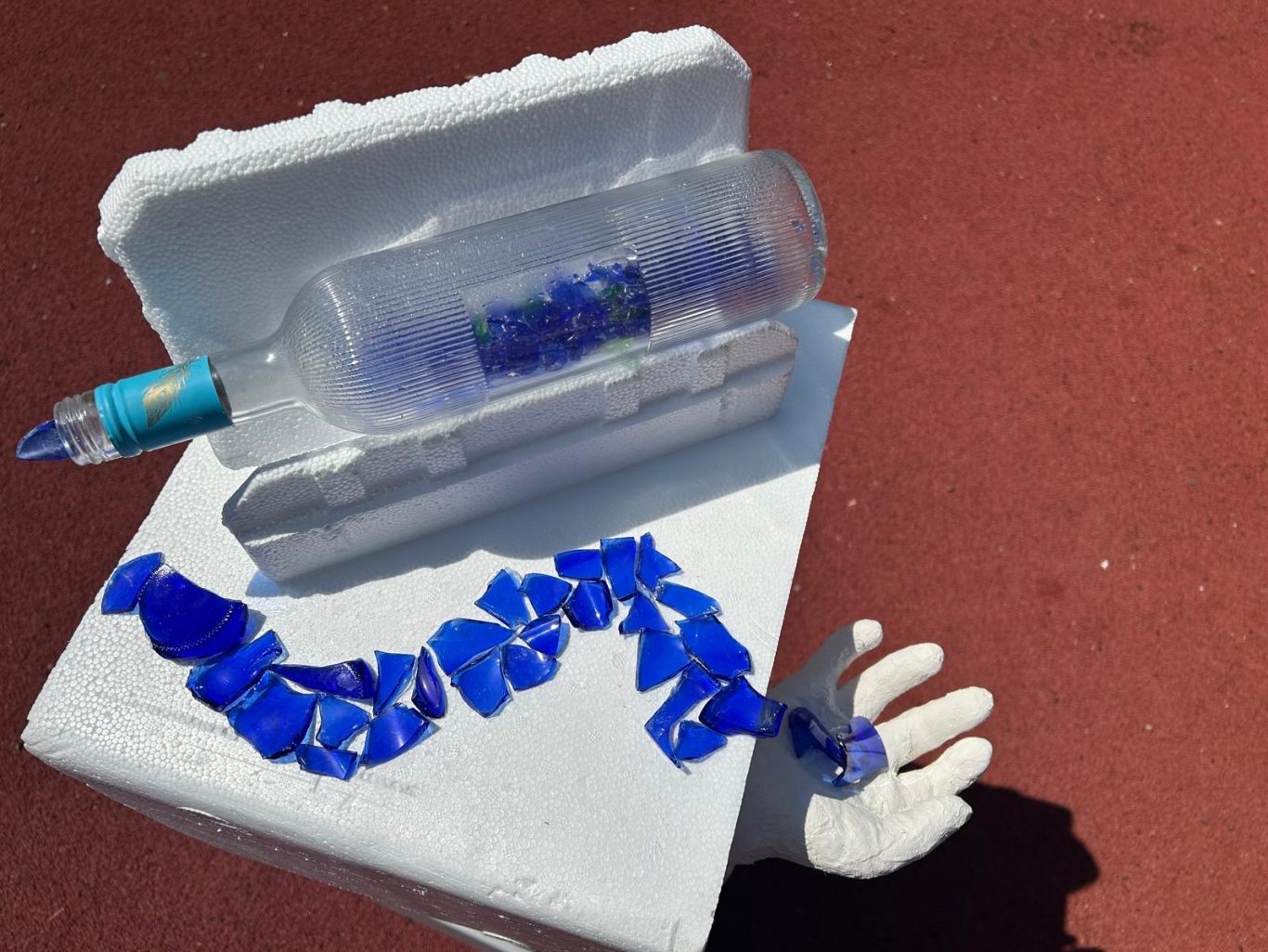 Eine durchsichtige Flasche liegt auf einem Styroporblock, umgeben von blauen Plastikstücken.