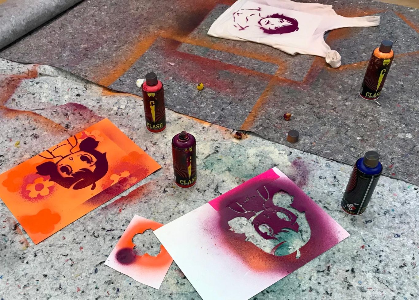 Sprühfarben und Schablonen mit grafischen Designs liegen auf einem grauen Untergrund.