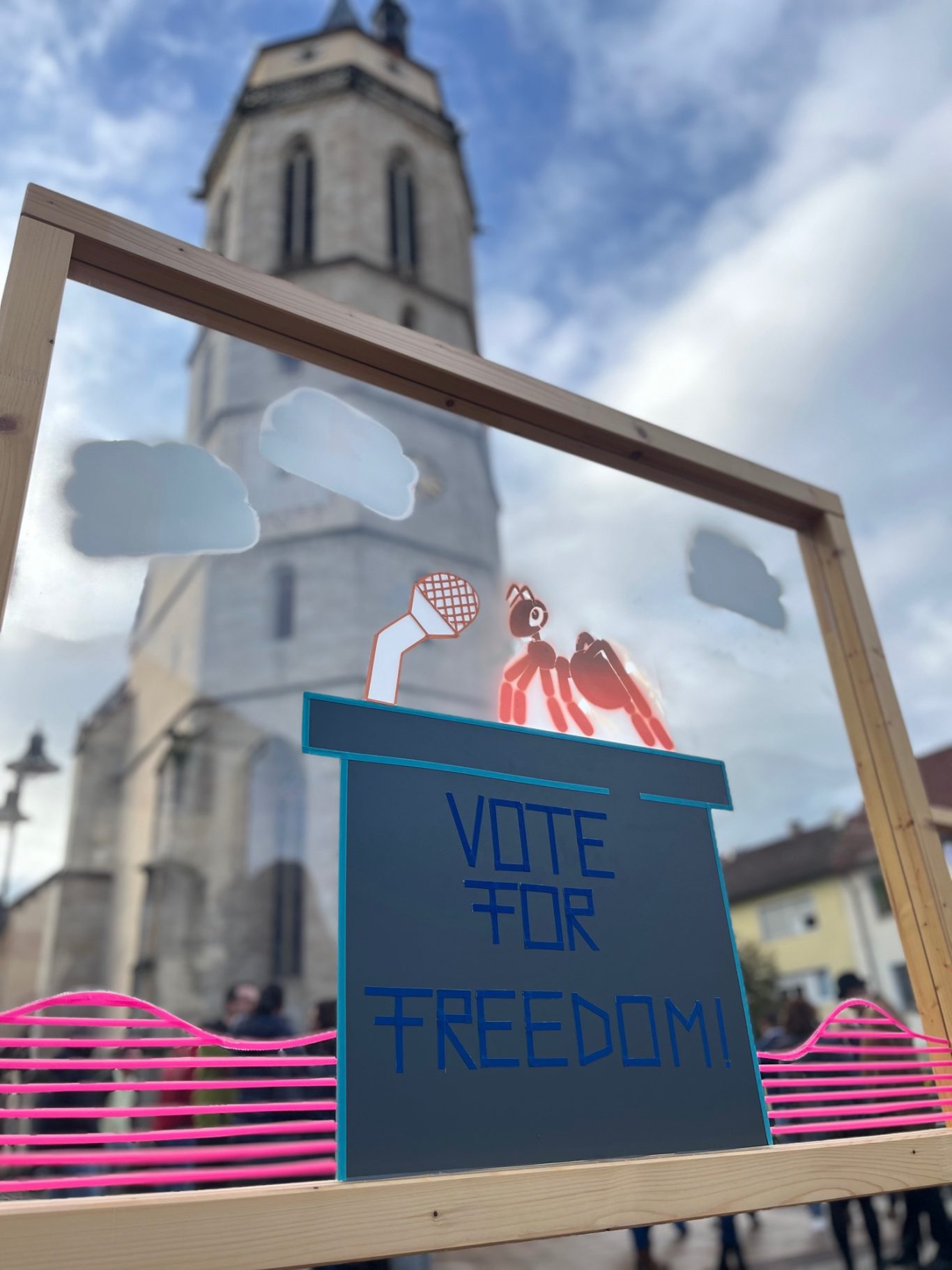 Wahlurne mit der Aufschrift "Vote for Freedom" vor einer Kirche und bewölktem Himmel.