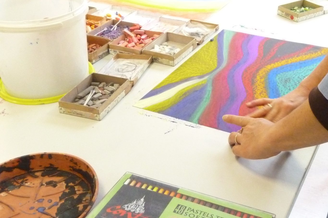 Bunte farbige Pastellzeichnungen auf einem Tisch mit verschiedenen Kunstmaterialien.