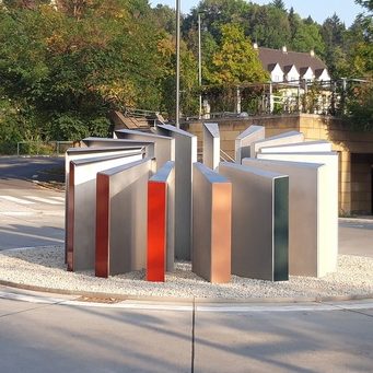 Skulptur aus mehreren stilisierten Buchformen in einem Außenbereich in einem Kreisverkehr.