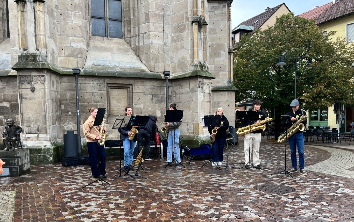Sechs Musiker mit Blasinstrumenten spielen vor einer historischen Gebäudewand.