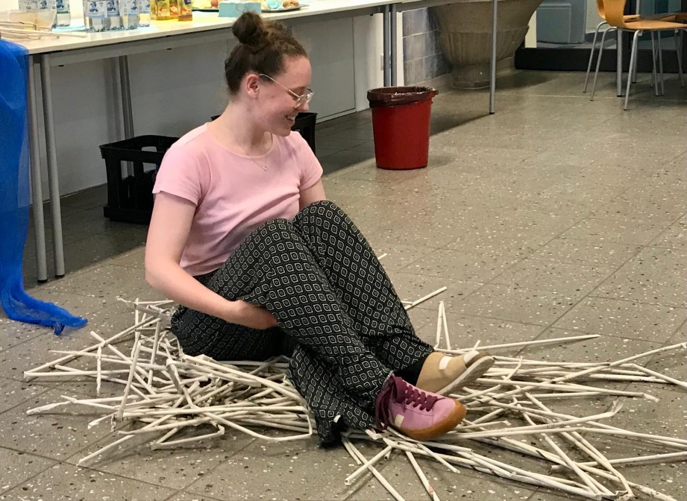 Eine Person sitzt lächelnd auf dem Boden, umgeben von Holzstäben.
