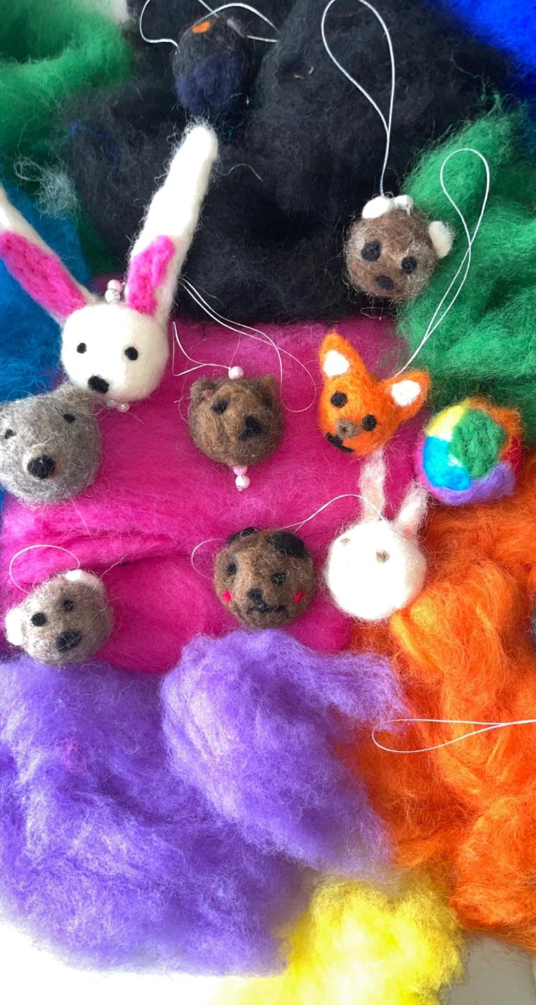 Bunte Filzkugeln in Tierform auf farbigem Wollhintergrund.