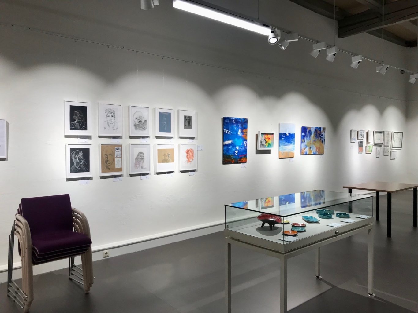 Moderne Galerie mit Kunstwerken an der Wand und einer Vitrine mit Objekten.