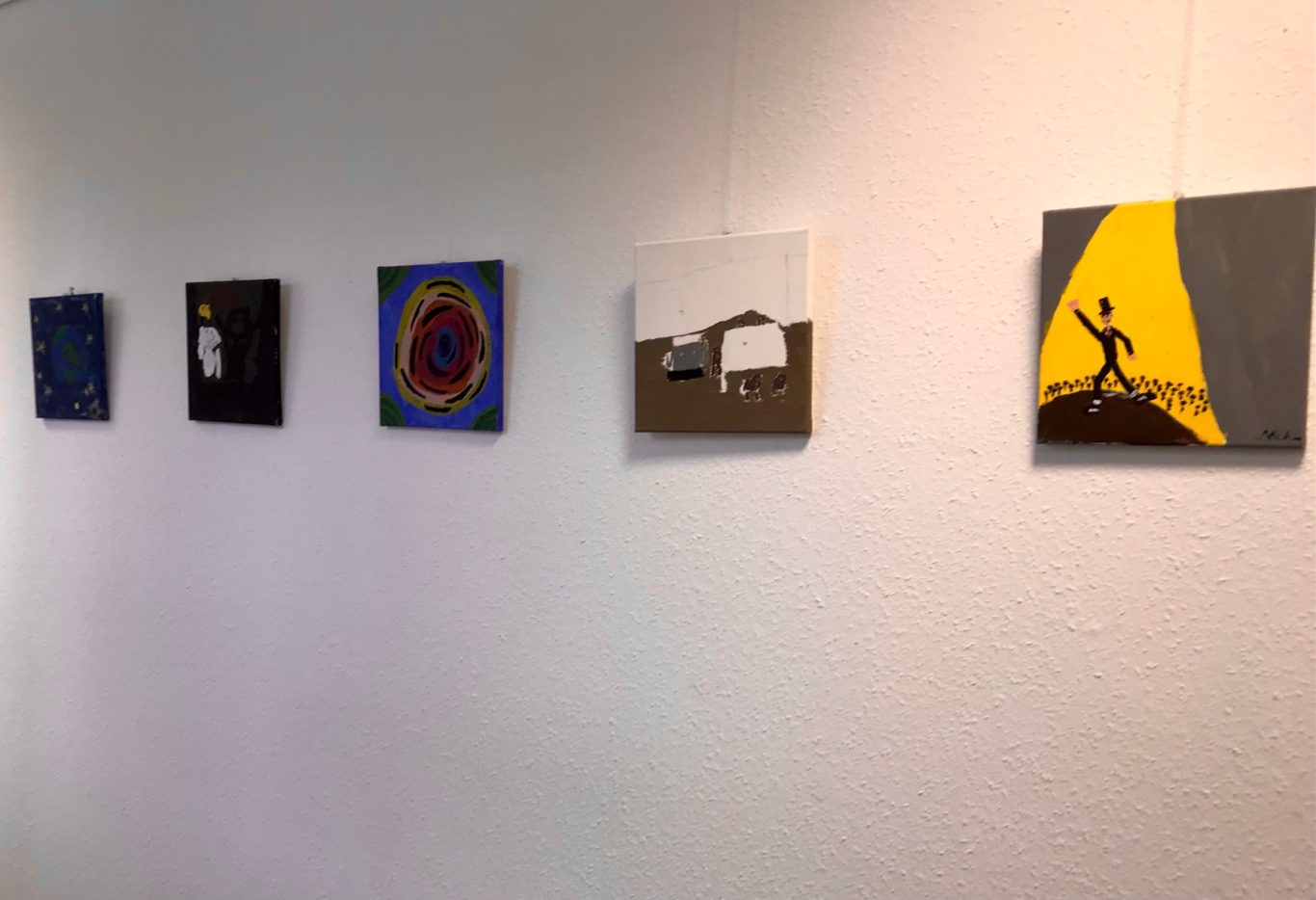 Eine Reihe von sechs Gemälden an einer weißen Wand in einer Galerie.