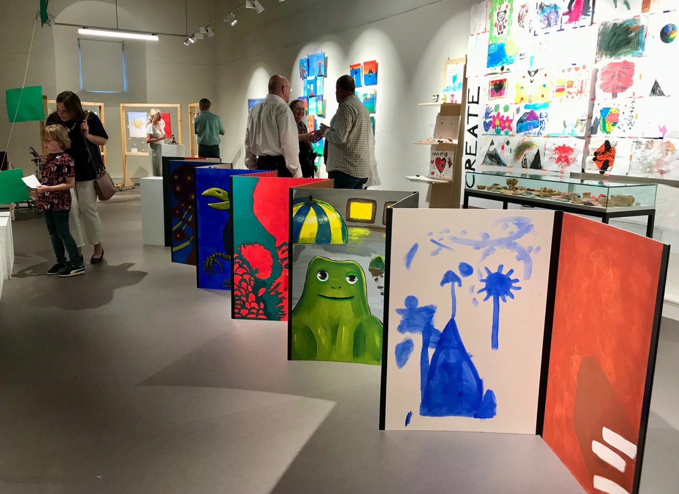 Ausstellung mit bunten Gemälden, Besucher betrachten die Kunstwerke im Hintergrund.