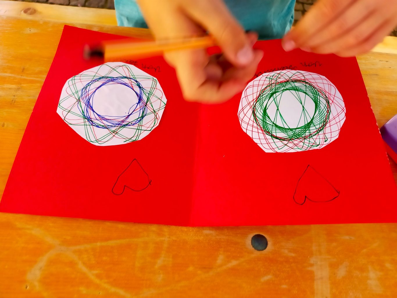 Zwei rote Seiten mit geometrischen Mustern, eine Hand hält einen Bleistift.