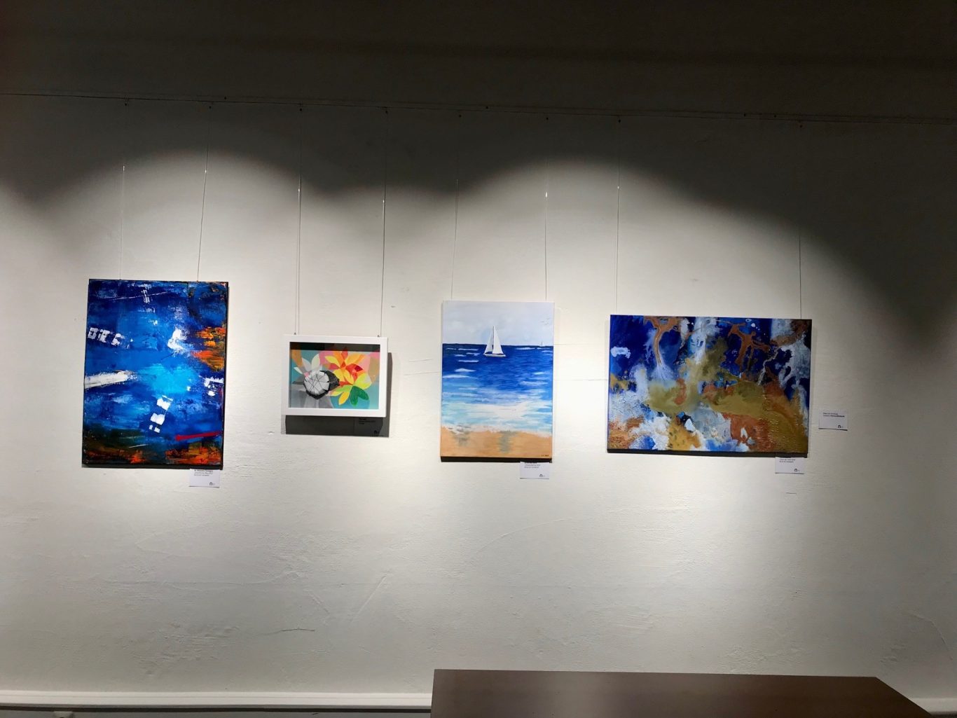 Vier Bilder in verschiedenen Farben und Stilen an einer beleuchteten Wand.