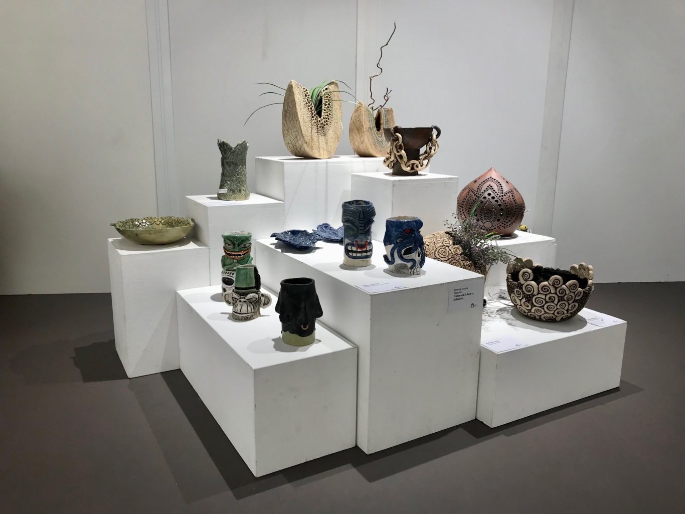 Verschiedene kunsthandwerkliche Töpferwaren auf weißen Ausstellungstischen.