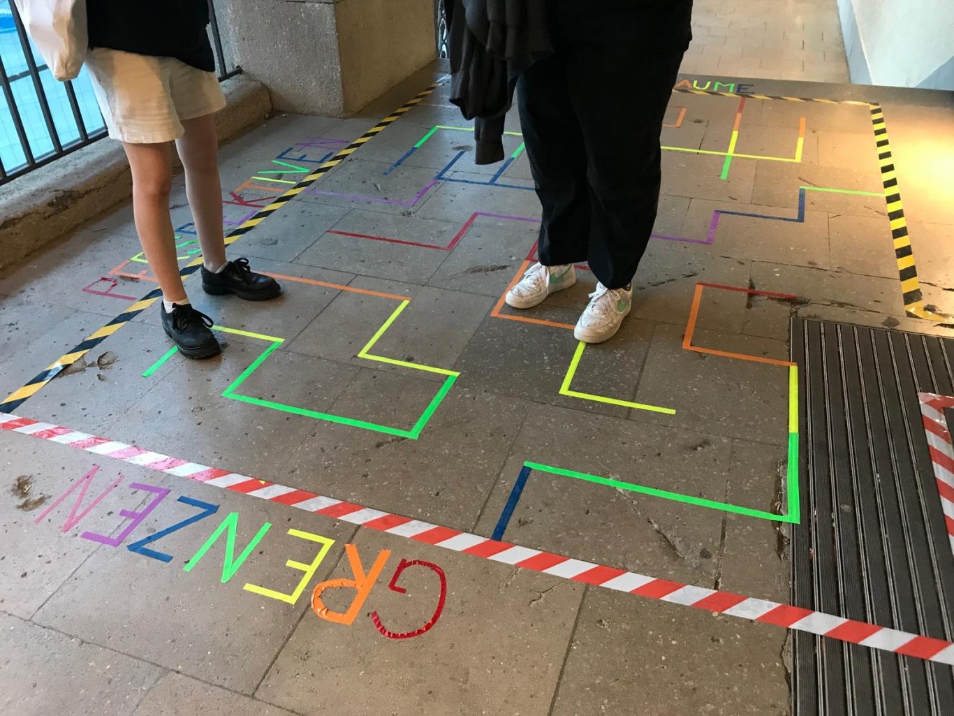Bunte Linien auf dem Boden bilden ein Zickzack-Muster mit der Beschriftung "GRENZEN".