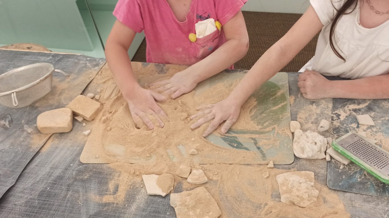 Zwei Kinder formen mit Händen kreativ einen sandigen Untergrund.